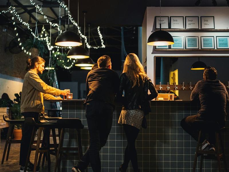 A young romantic couple consider the beer options at the dimly lit bar