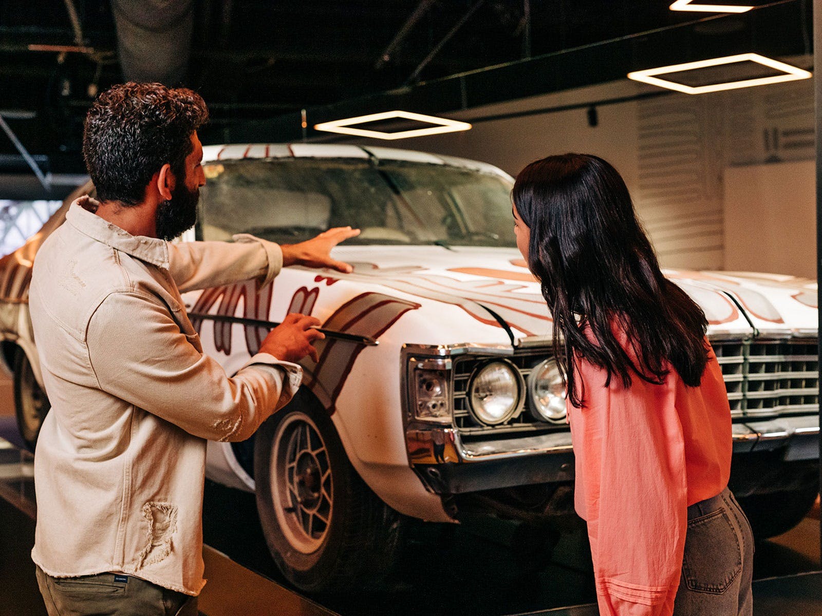 A man gestures at a car, as a young woman looks on