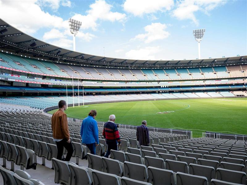 Four men walking through the stands to the ground of the MCG