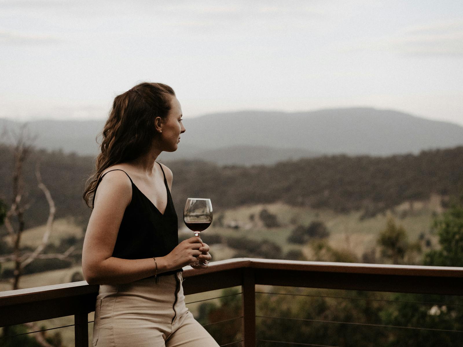 A women standing on the balcony with a red wine in hand looking at the mountain views