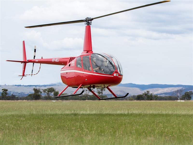 Red helicopter flying over grassy field