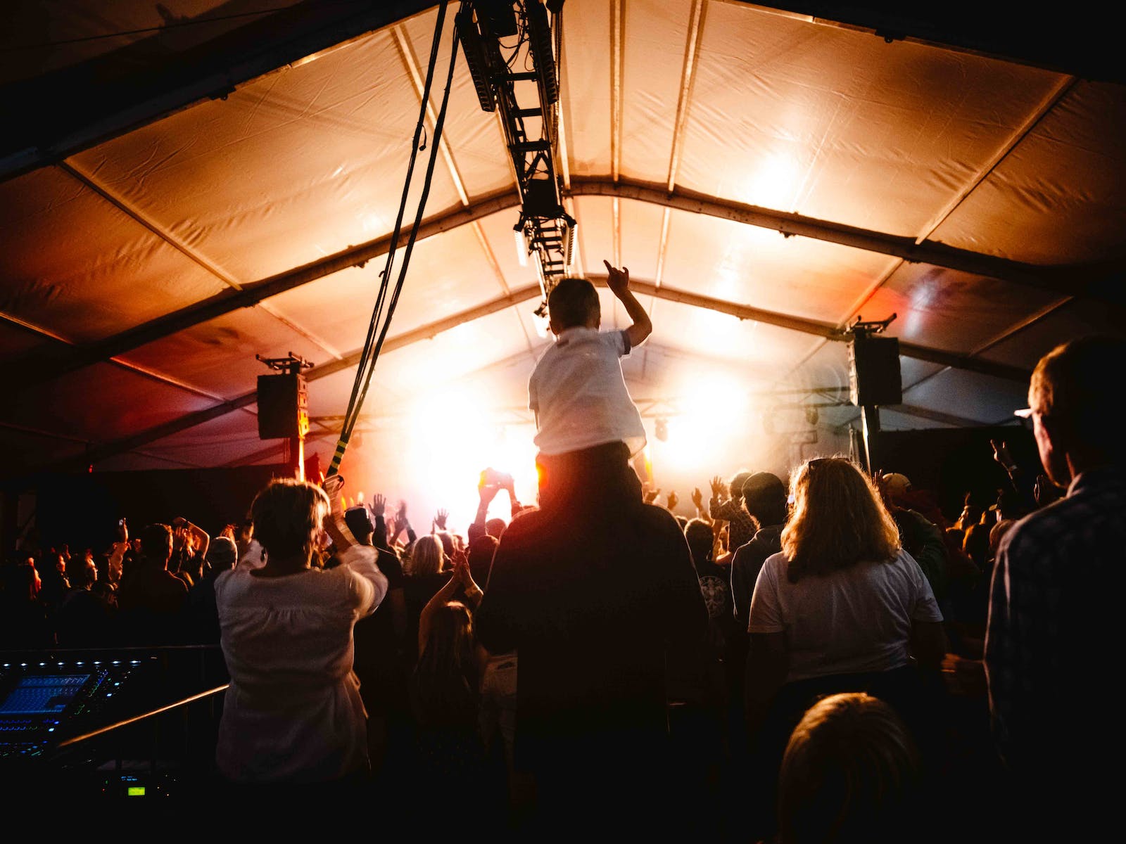 A child on the shoulder of an adult is watching music in a crowd.